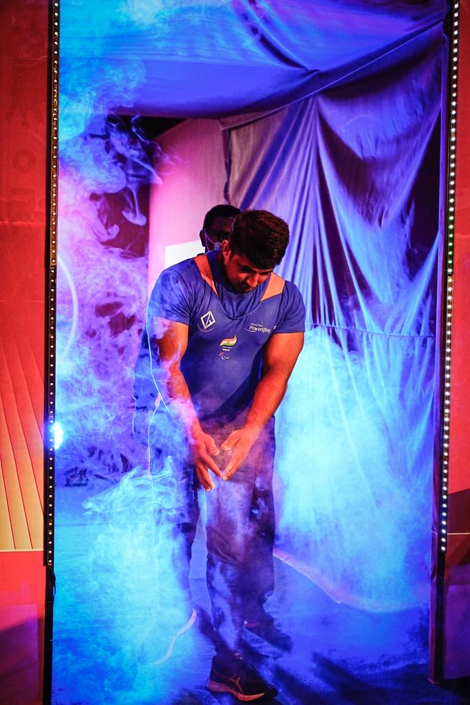 Para powerlifter in a blue national uniform entering through competition smoke