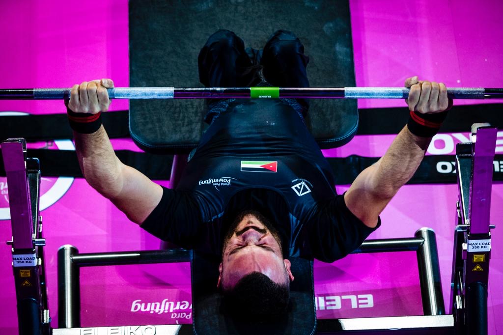 Jordanian para powerlifter in a black national uniform gripping the bar