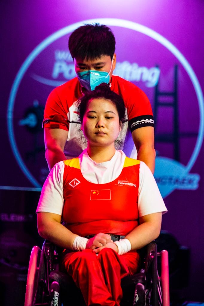 Chinese para powerlifter wearing a red national suit with their coach
