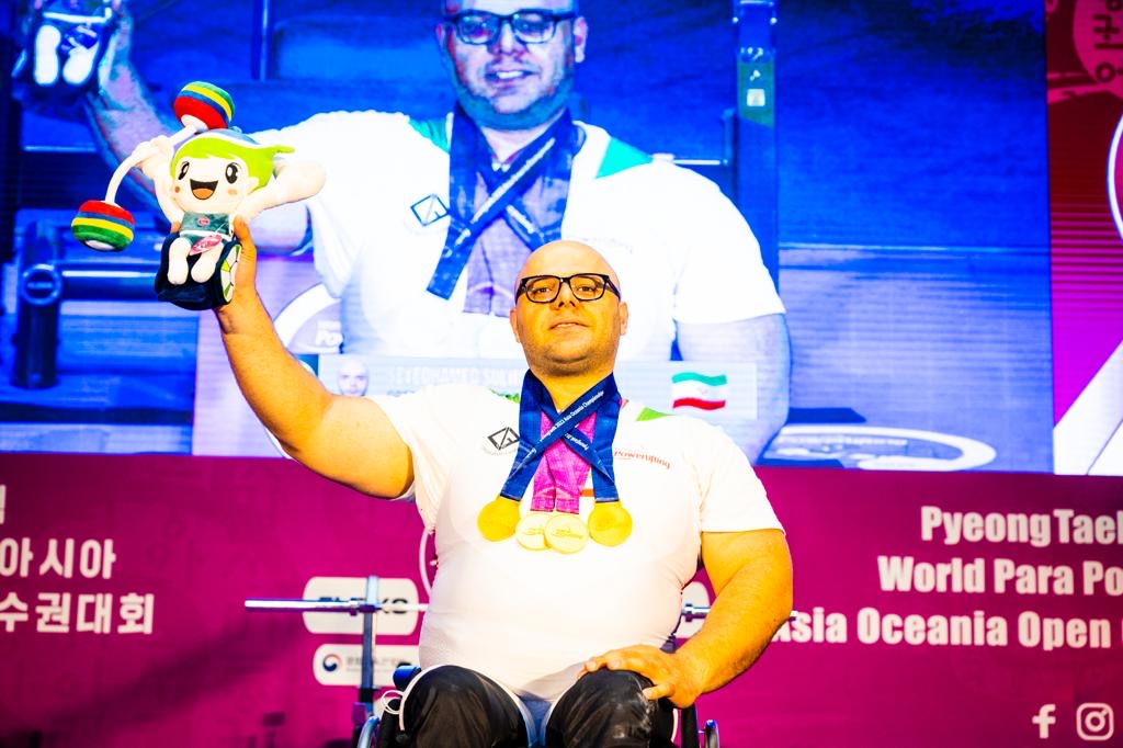 Medal-winning para powerlifter in a white national shirt holding the event mascot