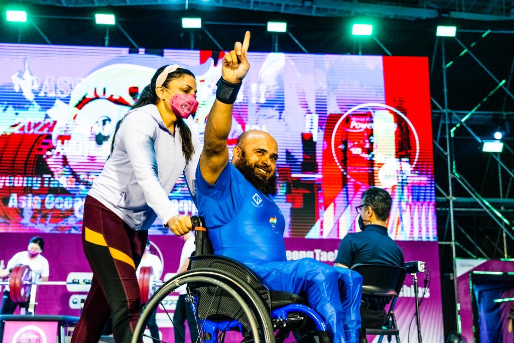 Para powerlifter in a blue national uniform celebrating from his wheelchair