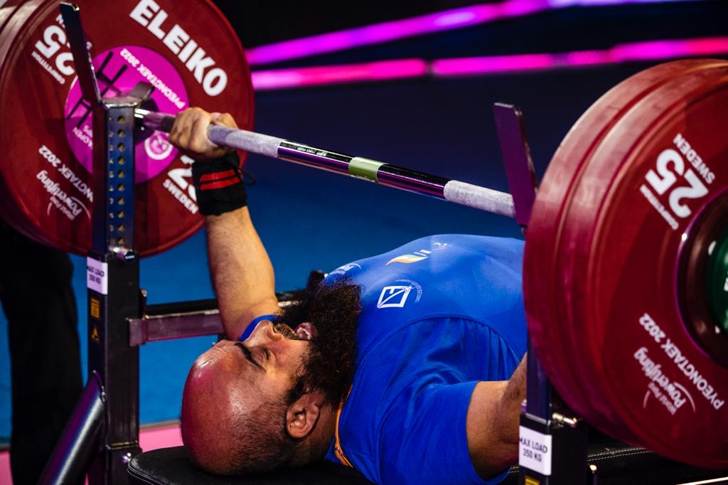 Para powerlifter wearing a blue competition uniform lifting a loaded bar