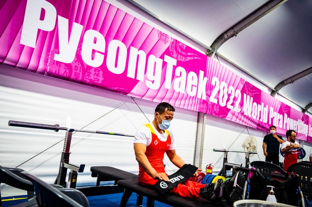 Para powerlifter wearing a red and white uniform in the warm-up area