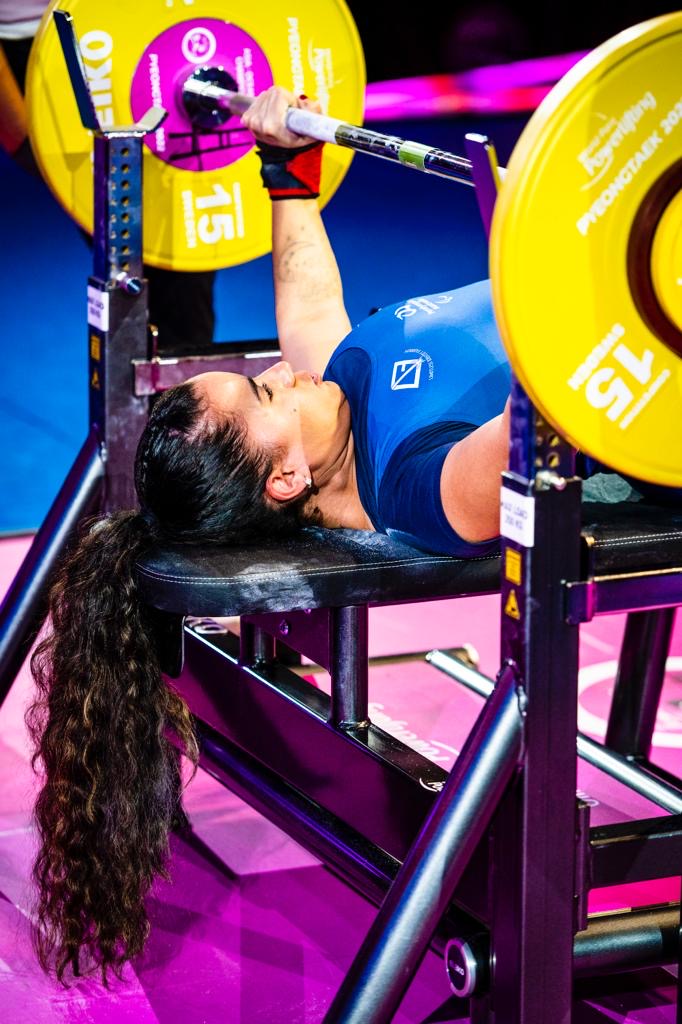 Female para powerlifter in a blue competition uniform lifting among yellow plates
