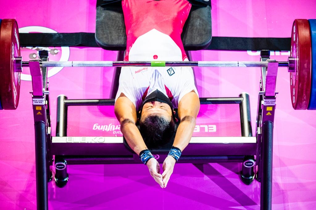 Para powerlifter in a red and white national suit preparing beneath the bar
