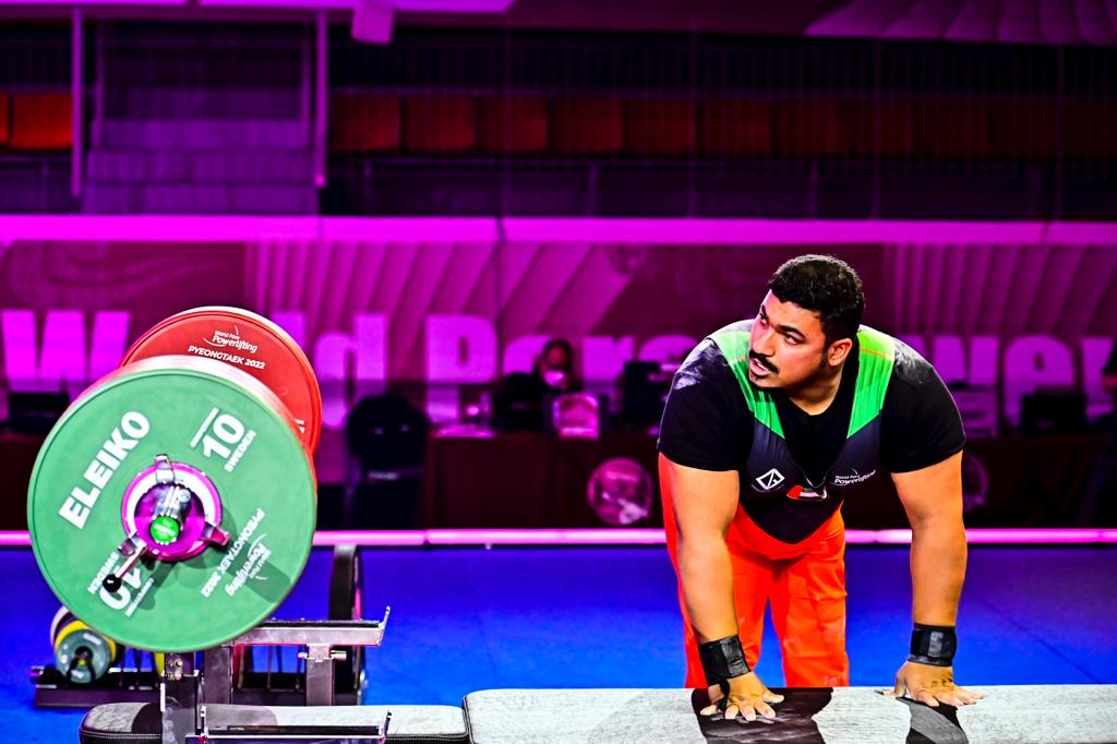 Para powerlifter in a black, green and red competition uniform beside a loaded bar
